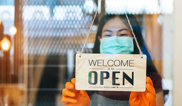 woman holding "welcome open" sign